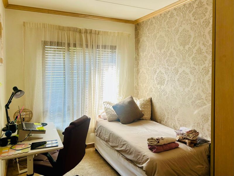 A cozy bedroom featuring patterned wallpaper, crown molding, and venetian blinds, providing a functional space with built-in storage.