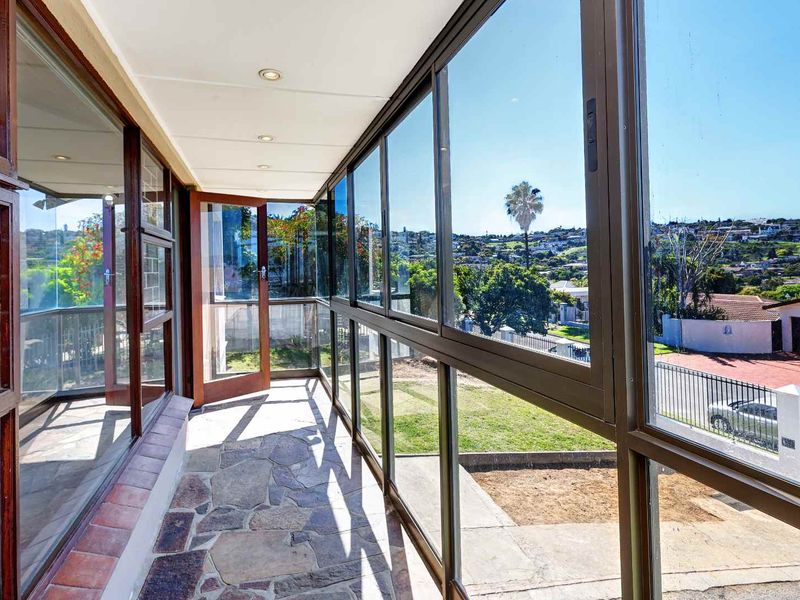 An enclosed sunroom or patio featuring stone flooring, recessed lighting, and expansive glass windows offering elevated views of the surrounding neighborhood.