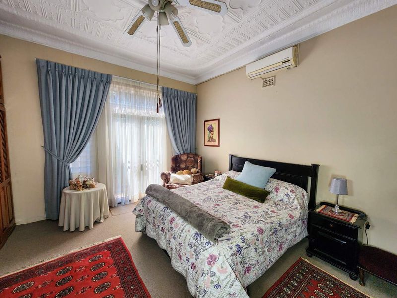 A spacious bedroom featuring a decorative plaster ceiling, ceiling fan, split system air conditioning, and direct access to an outdoor area via sliding glass doors.