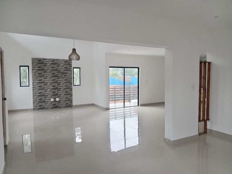 Spacious open-plan living area featuring polished tiled floors, a decorative stone-cladding feature wall, and large sliding glass doors leading to an outdoor space.