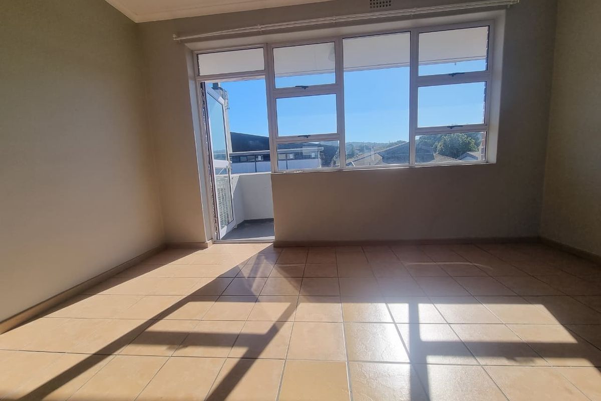 A bright, empty living area featuring neutral tiled flooring and large windows with direct access to a private balcony.
