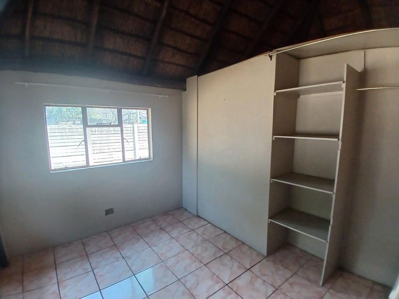 An empty bedroom featuring tiled flooring, a built-in wardrobe, and a distinctive exposed thatched roof ceiling.