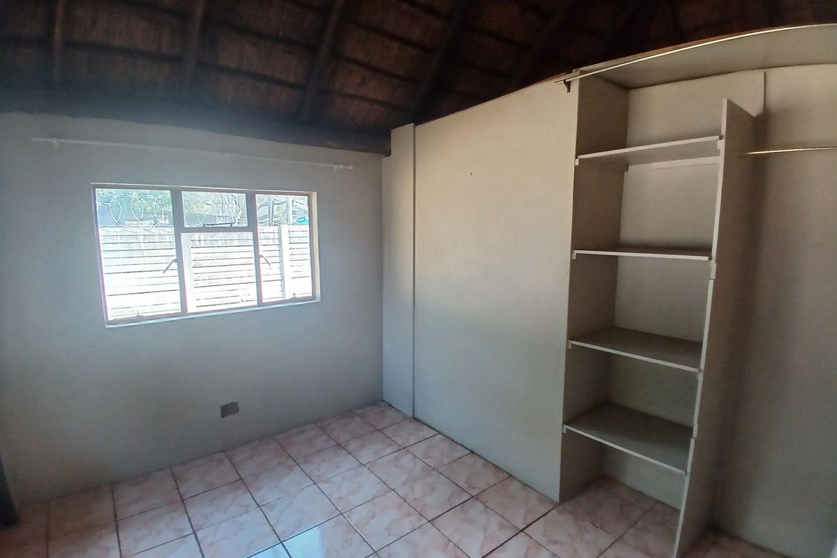 An empty bedroom featuring tiled flooring, a built-in wardrobe, and a distinctive exposed thatched roof ceiling.