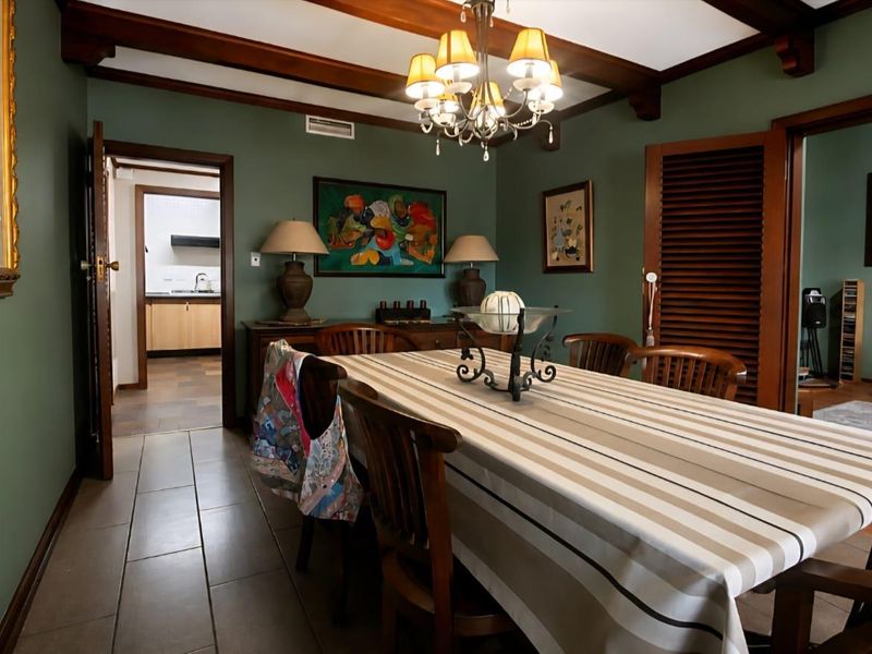 A formal dining room featuring exposed timber ceiling beams, tiled flooring, and a classic chandelier, with direct access to the kitchen and living area.