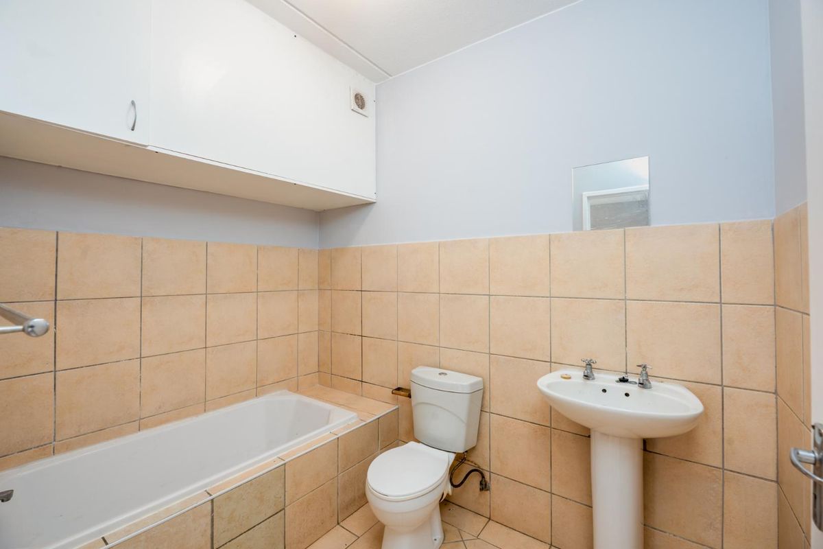 A functional bathroom featuring a tiled bathtub, pedestal basin, and toilet with wall-mounted storage cabinetry.