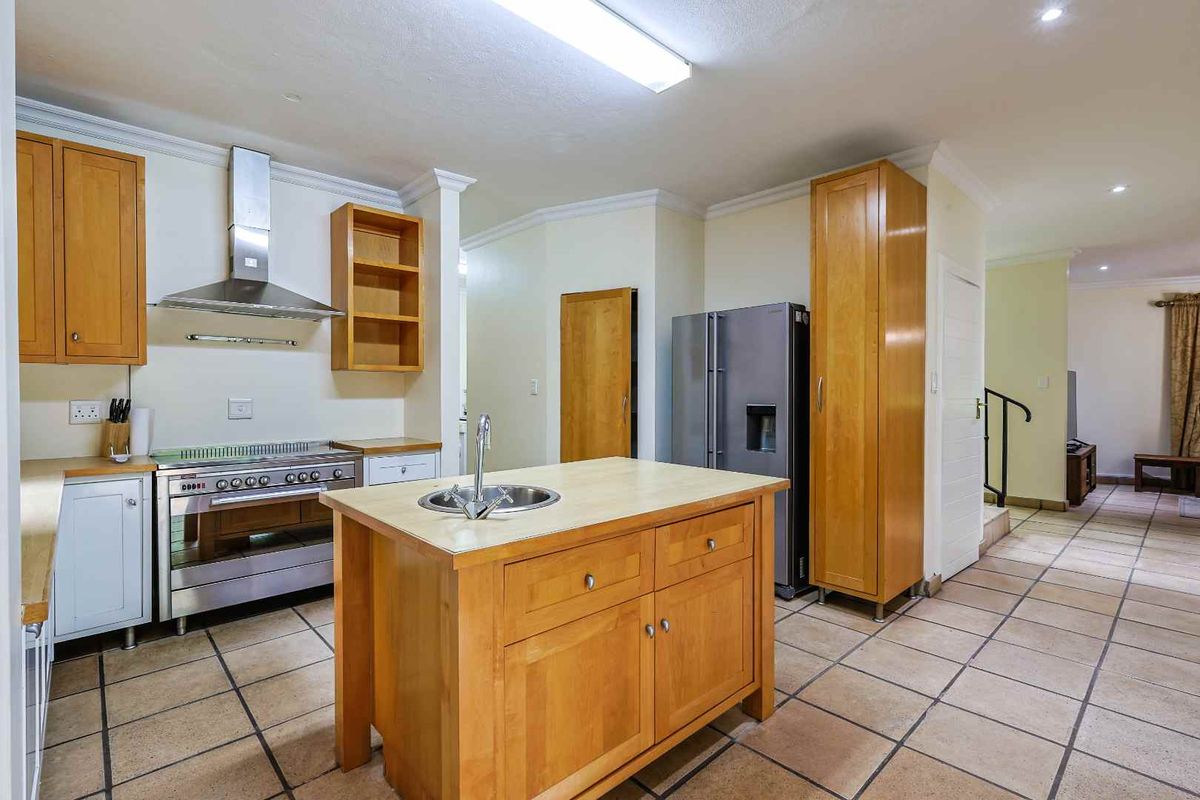 A functional kitchen featuring wooden cabinetry, a central island with a prep sink, stainless steel stove, and tiled flooring.