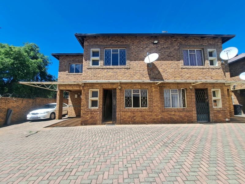 Front elevation of a double-story face brick townhouse featuring a paved driveway, carport, and secure entrance.