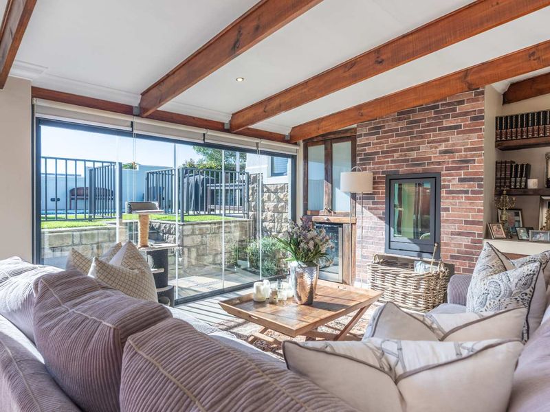 A cozy living room featuring exposed timber ceiling beams, a brick fireplace wall, and large sliding glass doors opening to an outdoor patio area.