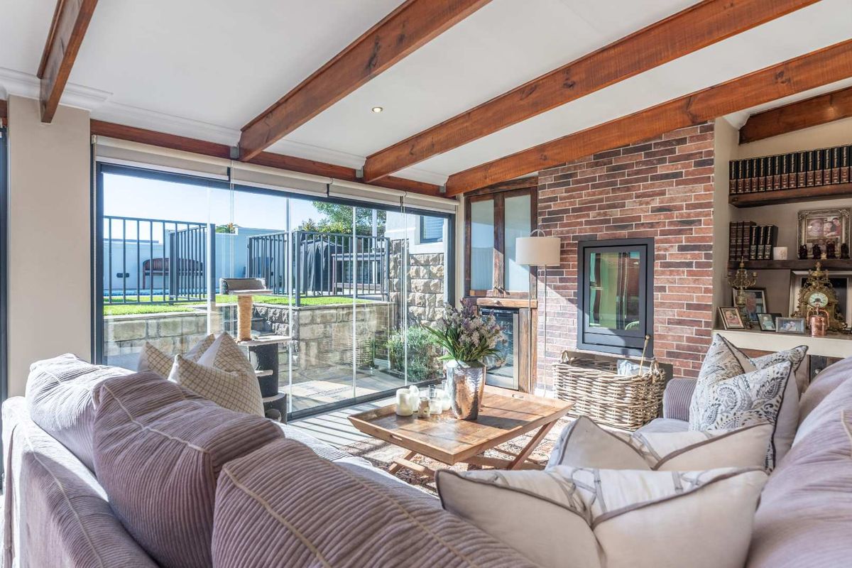 A cozy living room featuring exposed timber ceiling beams, a brick fireplace wall, and large sliding glass doors opening to an outdoor patio area.
