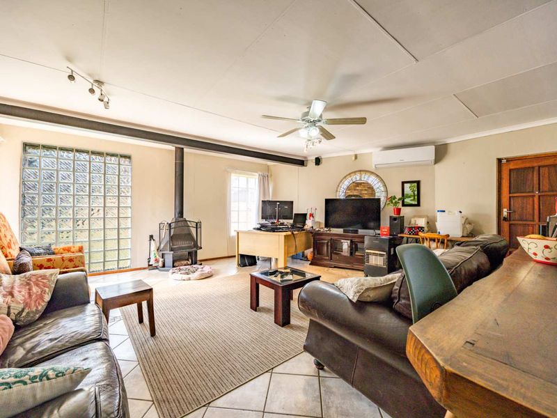 Spacious living room featuring a freestanding fireplace, glass block feature window, ceiling fan, and split-system air conditioning unit.