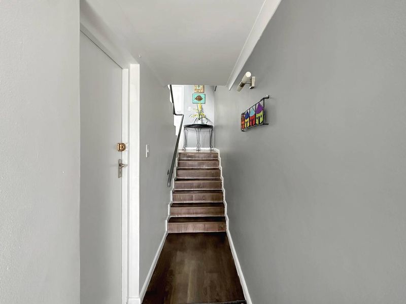 A clean, well-maintained hallway featuring dark laminate flooring, a staircase with a handrail, and neutral grey wall finishes.