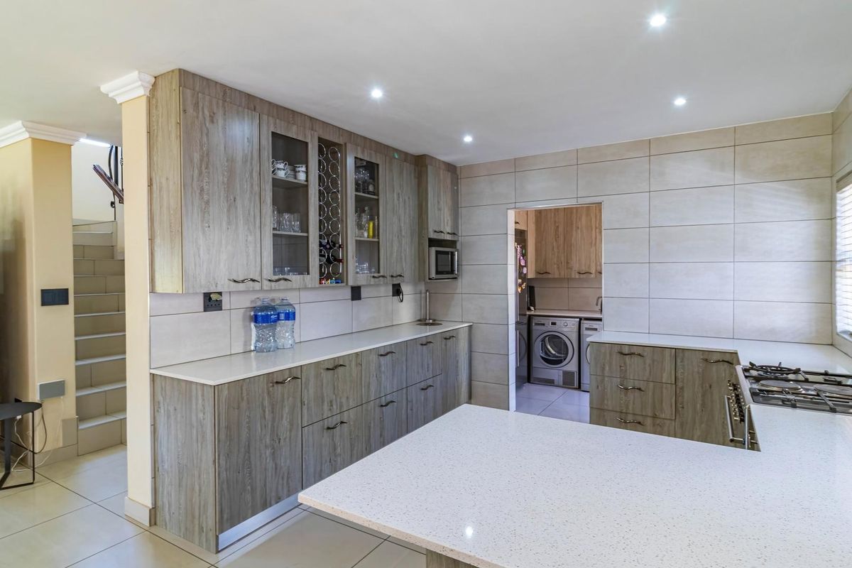 Modern kitchen featuring wood-grain cabinetry, stone countertops, a gas hob, and a convenient adjoining scullery area with laundry facilities.
