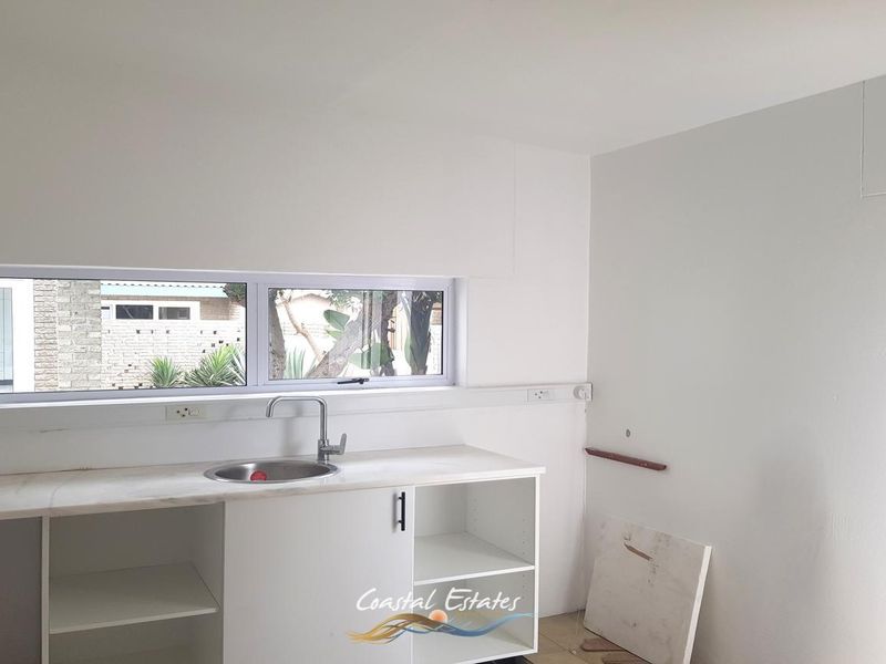A functional scullery or utility area featuring a stainless steel sink, built-in cabinetry, and a horizontal window, currently in need of minor finishing touches.