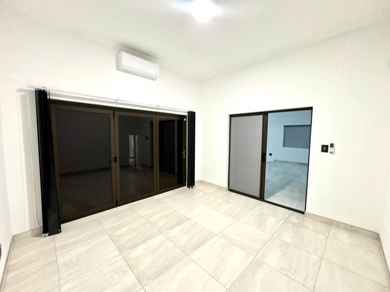A bright, empty living area featuring large aluminium sliding and folding doors, neutral tiled flooring, and a wall-mounted split-system air conditioner.