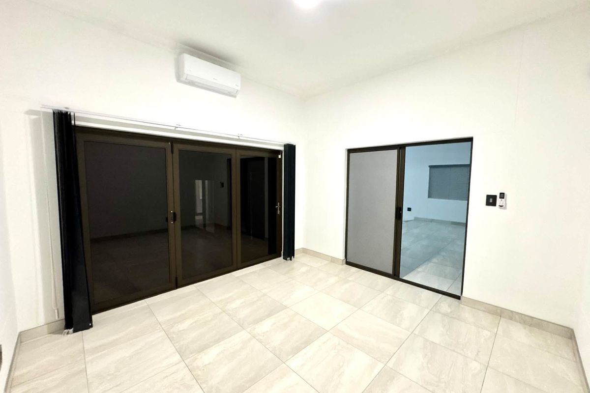 A bright, empty living area featuring large aluminium sliding and folding doors, neutral tiled flooring, and a wall-mounted split-system air conditioner.