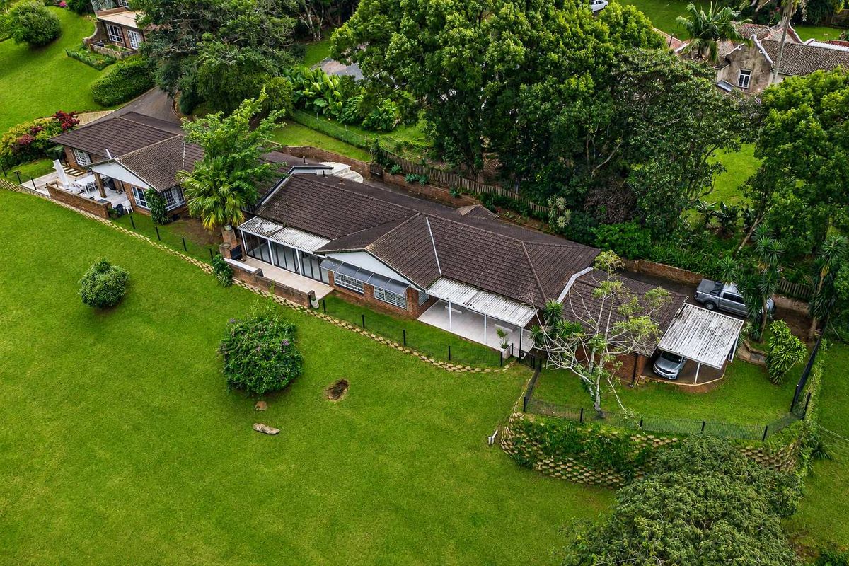 Aerial view of a townhouse property featuring a tiled roof, covered patio, carport, and extensive landscaped garden grounds.