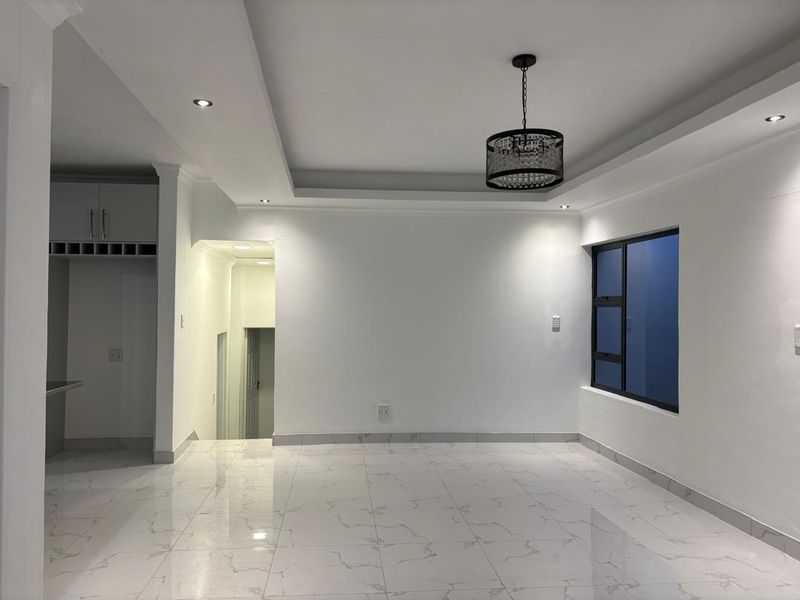 A bright, modern living area featuring polished marble-look floor tiles, a tray ceiling with recessed lighting, and a contemporary pendant light fixture.