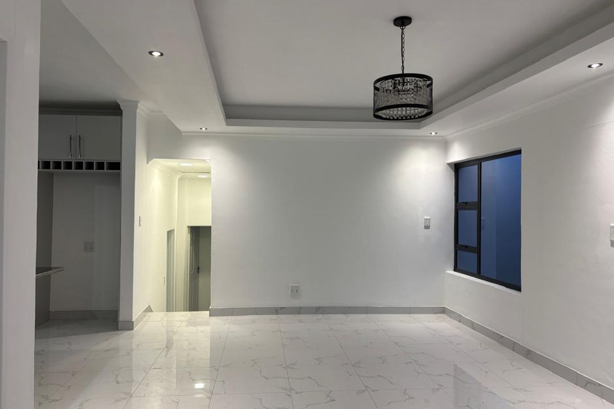 A bright, modern living area featuring polished marble-look floor tiles, a tray ceiling with recessed lighting, and a contemporary pendant light fixture.