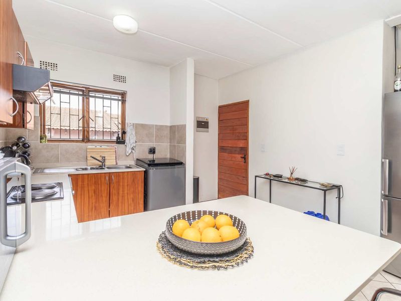 A functional kitchen featuring wood-finish cabinetry, tiled backsplash, integrated hob, extractor fan, and a central island with ample counter space.
