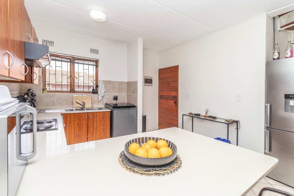 A functional kitchen featuring wood-finish cabinetry, tiled backsplash, integrated hob, extractor fan, and a central island with ample counter space.