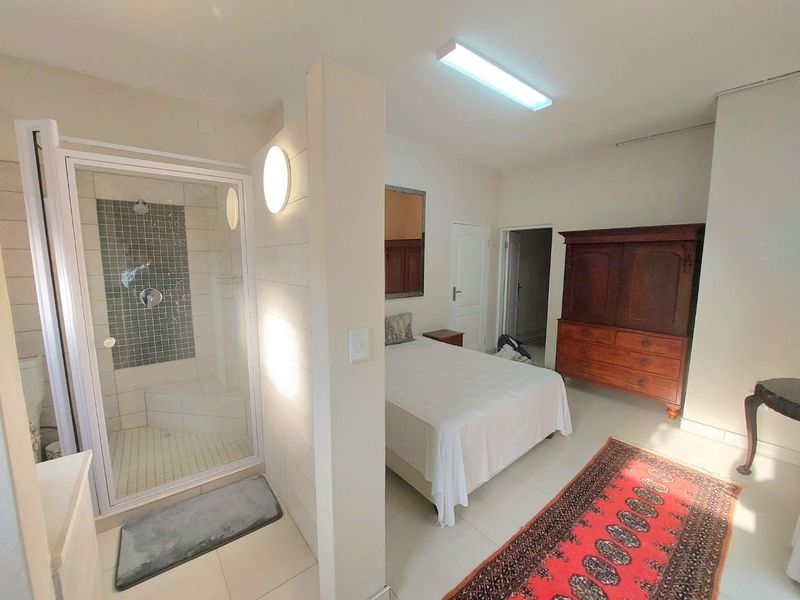 Bedroom featuring an open-plan en-suite shower with mosaic tiling, neutral wall finishes, and tiled flooring throughout.