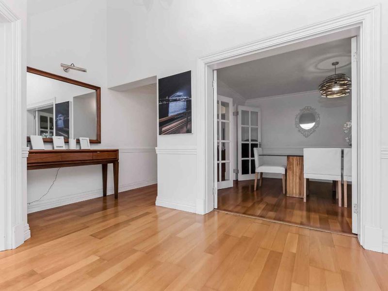 A bright and welcoming entrance hall featuring polished hardwood flooring, classic wainscoting, and elegant french doors leading into the dining area.