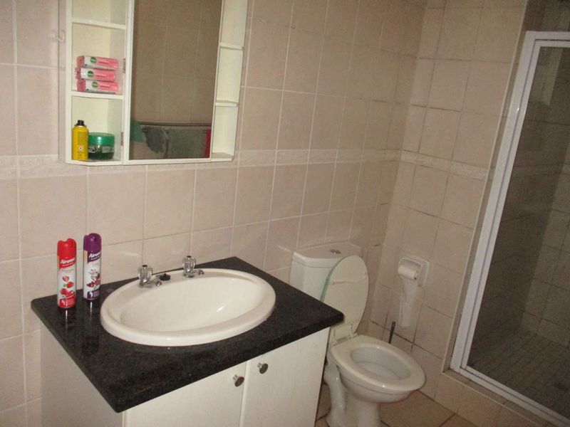 A functional bathroom featuring a vanity with granite countertop, integrated basin, toilet, and a separate shower enclosure with tiled walls.