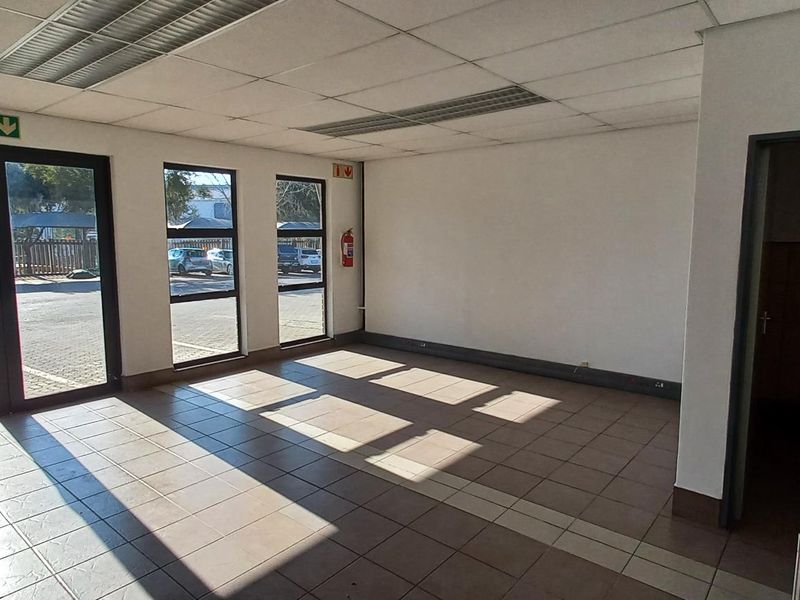 Open plan industrial office space featuring tiled flooring, suspended ceilings, large windows for natural light, and an integrated kitchenette area.