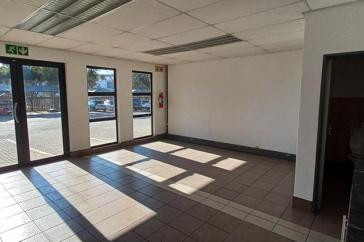 Open plan industrial office space featuring tiled flooring, suspended ceilings, large windows for natural light, and an integrated kitchenette area.