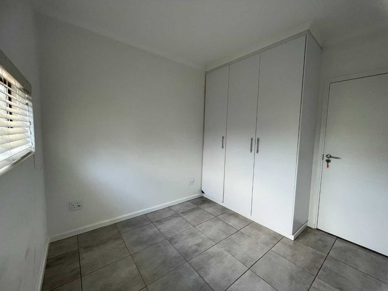 A clean, empty bedroom featuring neutral tiled flooring, built-in white cupboards, and venetian blinds, offering a versatile space ready for personalization.