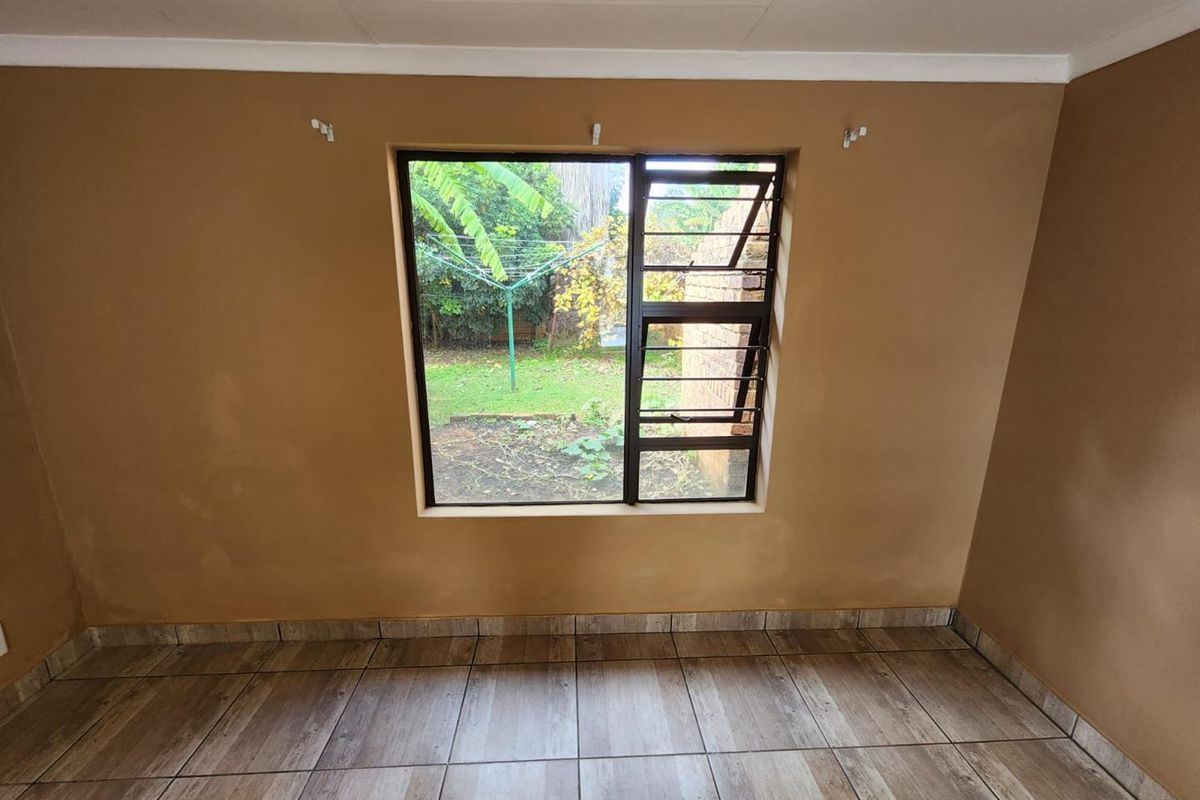 An empty bedroom featuring wood-look tiled flooring, a window with security bars, and plain painted walls.
