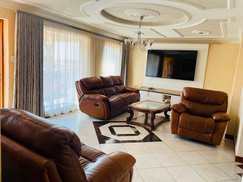 Spacious living room featuring decorative ceiling molding, tiled flooring, and a built-in media wall unit, offering a comfortable and well-maintained living space.
