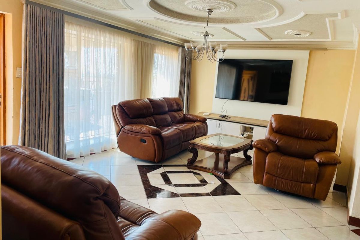 Spacious living room featuring decorative ceiling molding, tiled flooring, and a built-in media wall unit, offering a comfortable and well-maintained living space.