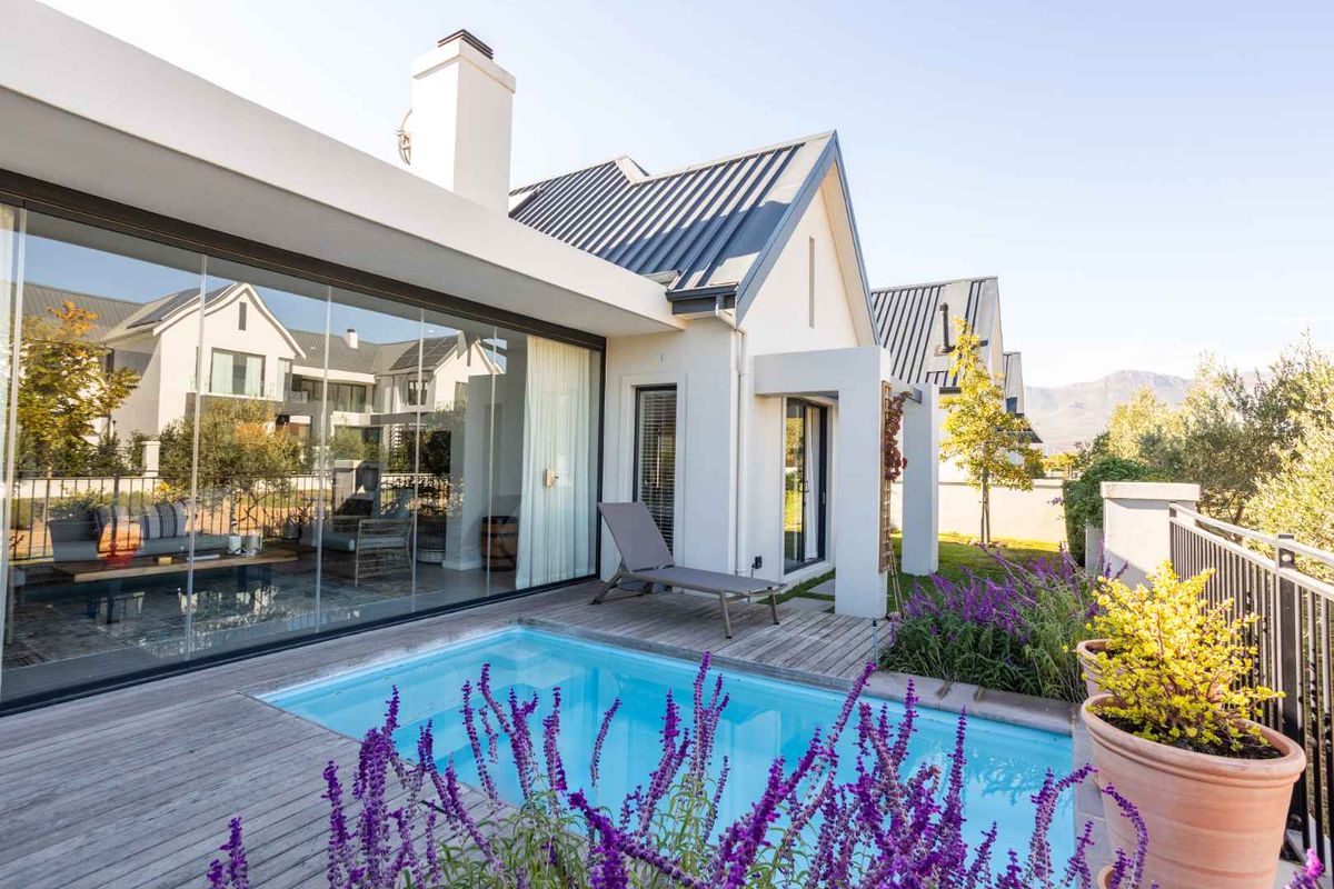 A modern rear exterior view featuring a private swimming pool, timber decking, and large glass sliding doors leading into the living area.