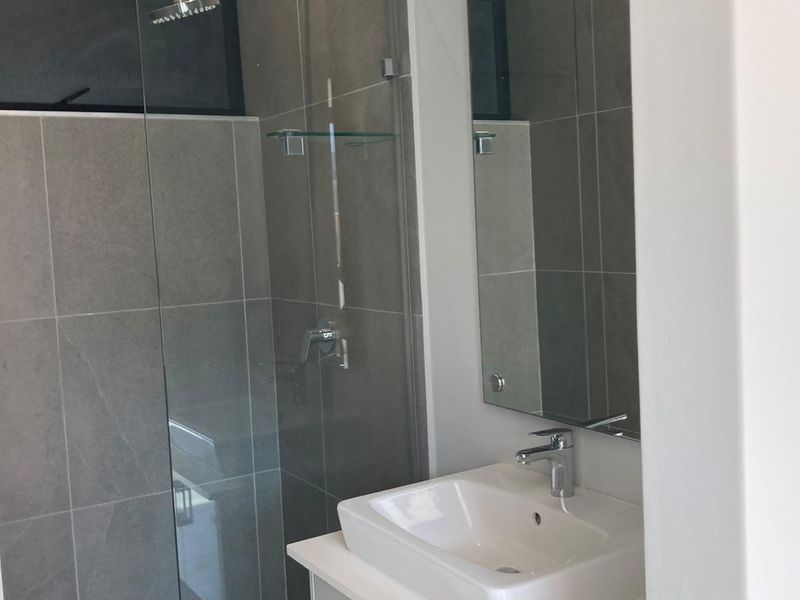 Modern bathroom featuring a glass-enclosed shower, contemporary vanity basin with chrome mixer tap, and neutral grey wall tiling.