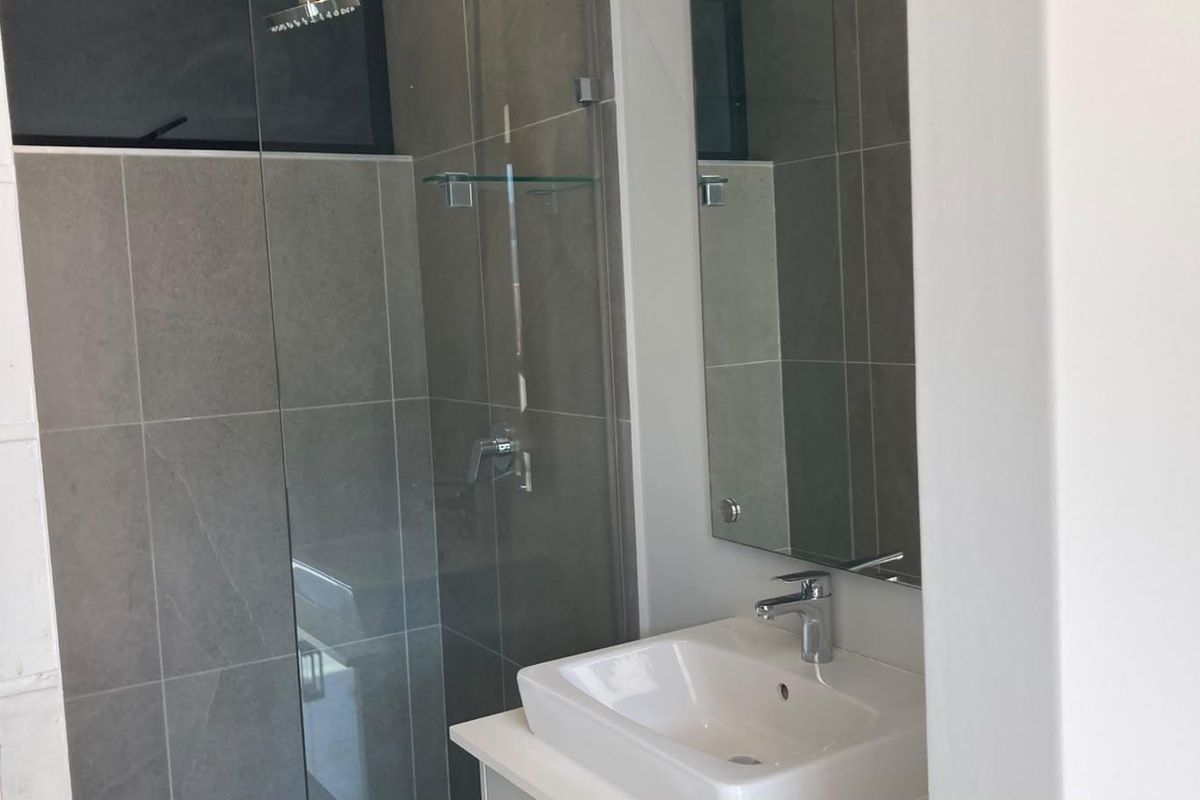 Modern bathroom featuring a glass-enclosed shower, contemporary vanity basin with chrome mixer tap, and neutral grey wall tiling.
