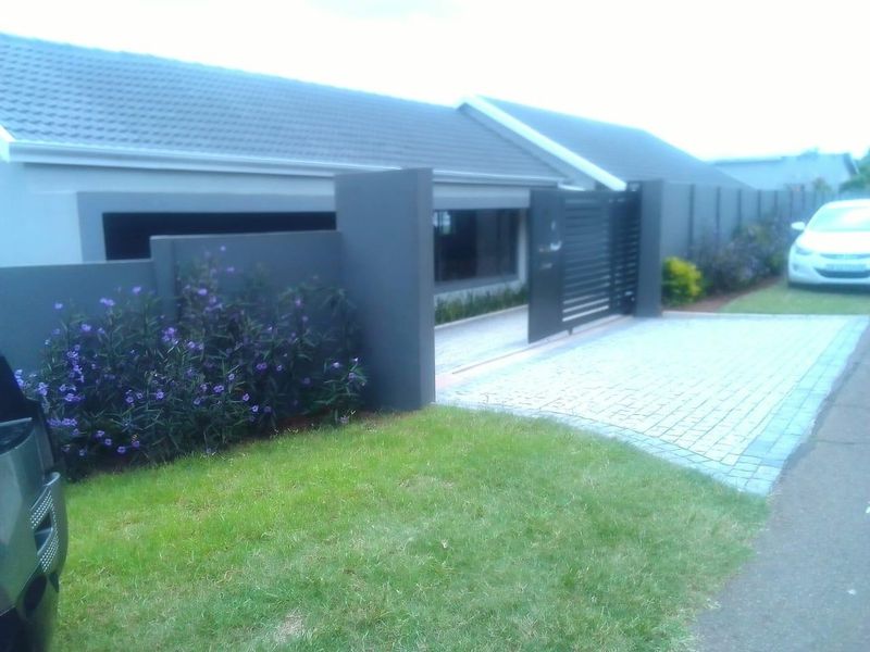Front view of the property featuring a paved driveway, modern boundary wall, and a sliding gate entrance.