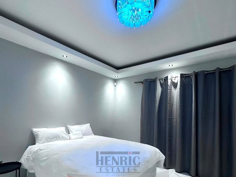 A modern bedroom featuring recessed ceiling lighting, cove lighting, and tiled flooring.
