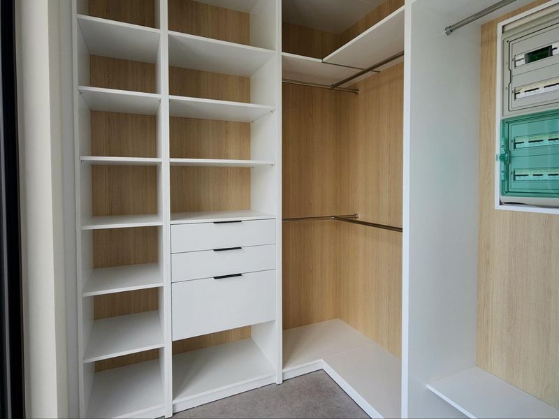 A modern, empty walk-in closet featuring custom built-in cabinetry with white and wood-grain finishes, including shelving, drawers, and hanging rails.