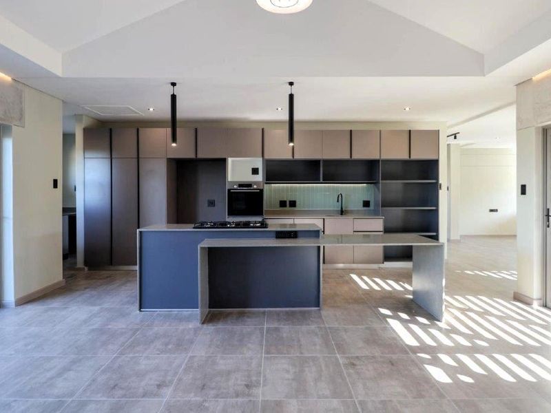 Modern, spacious kitchen featuring sleek built-in cabinetry, a central island with a gas hob, integrated appliances, and large format floor tiles.