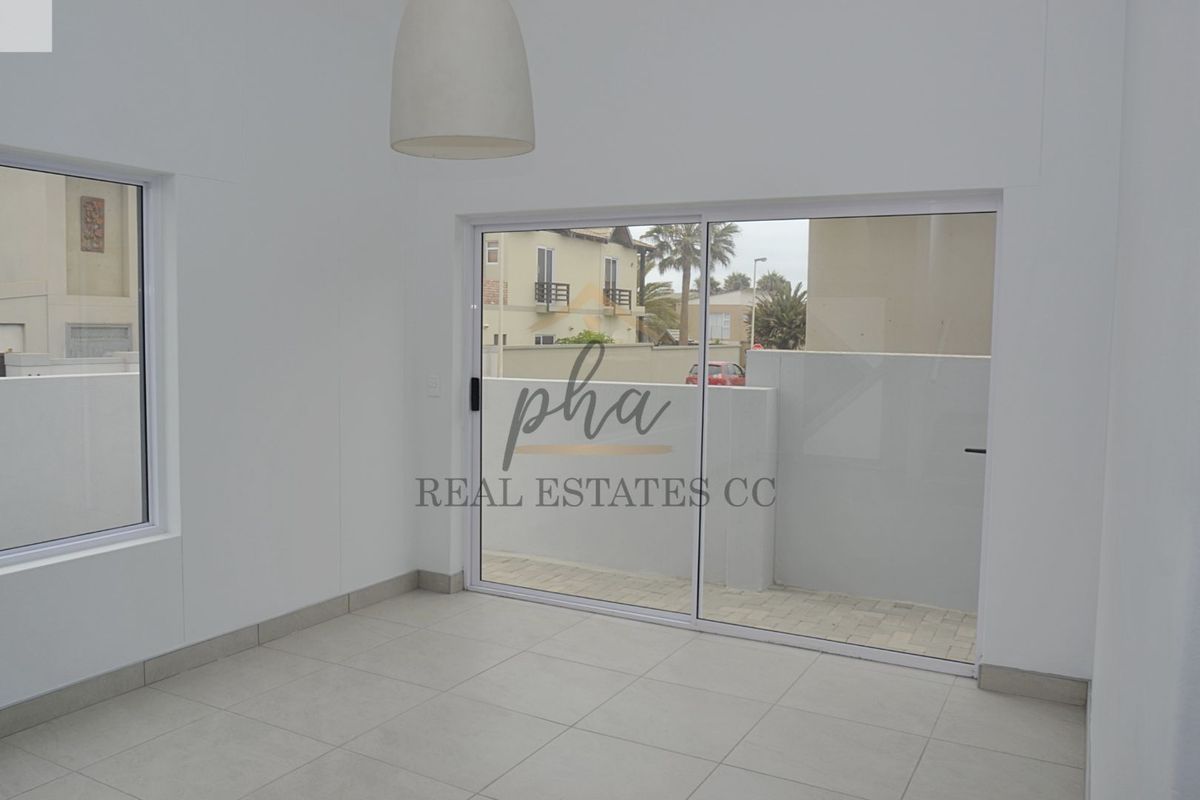 A bright, empty living area featuring large sliding glass doors that open onto a paved patio space.