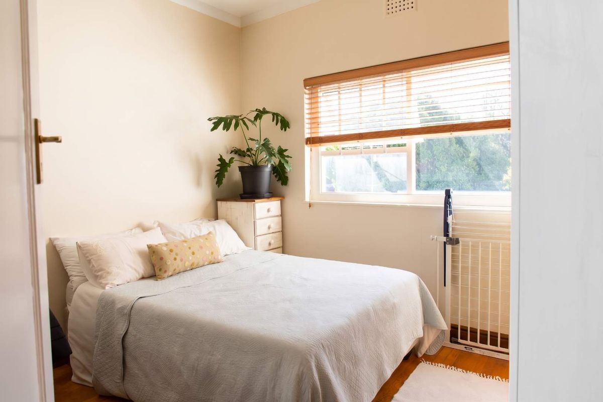 A cozy bedroom featuring timber flooring, neutral wall tones, and a window fitted with timber venetian blinds, providing natural light.