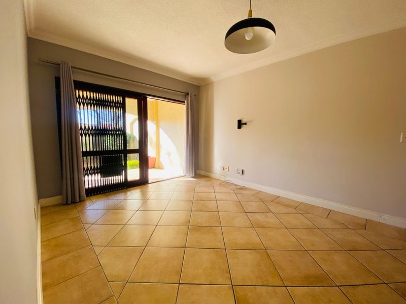 An empty living room featuring ceramic floor tiles, a sliding glass door with a security gate, and access to an outdoor patio area.