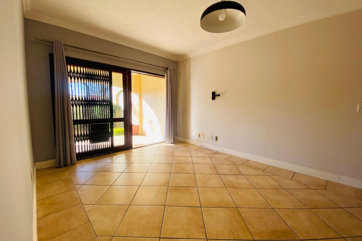 An empty living room featuring ceramic floor tiles, a sliding glass door with a security gate, and access to an outdoor patio area.