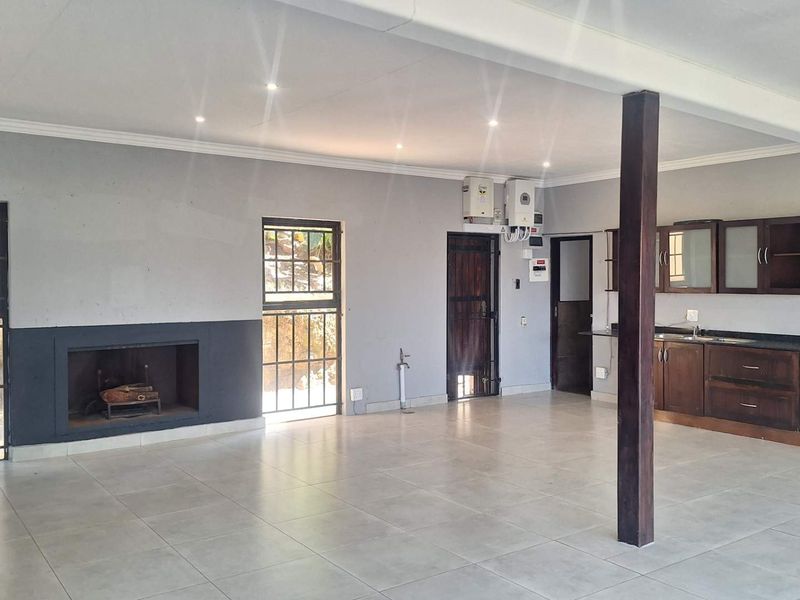 Spacious open-plan living area featuring a built-in fireplace, tiled flooring, and a functional kitchen with dark wood cabinetry and integrated appliances.