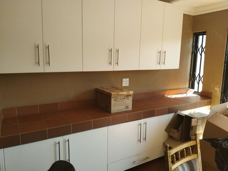 A functional scullery or utility area featuring white built-in cabinetry, tiled countertops, and a window with security bars.