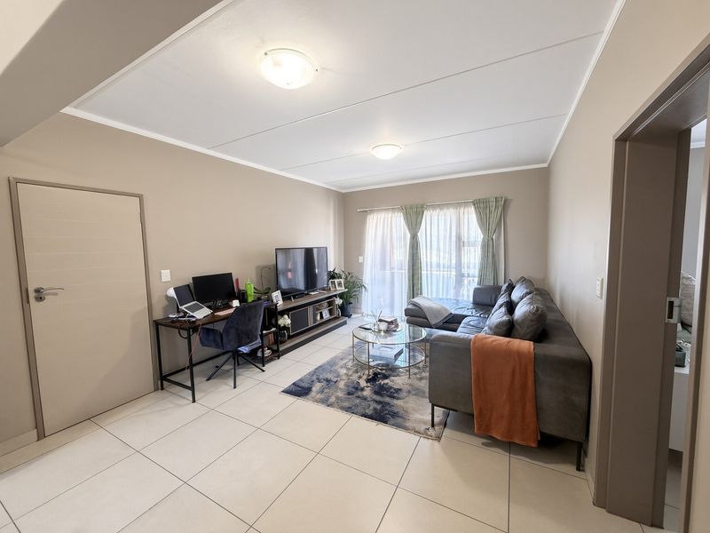 A well-maintained living room featuring neutral wall tones, large format floor tiles, and a sliding glass door providing natural light.