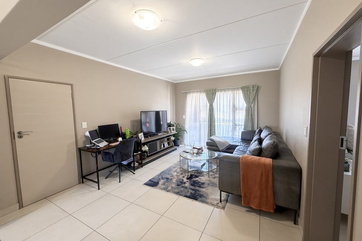 A well-maintained living room featuring neutral wall tones, large format floor tiles, and a sliding glass door providing natural light.
