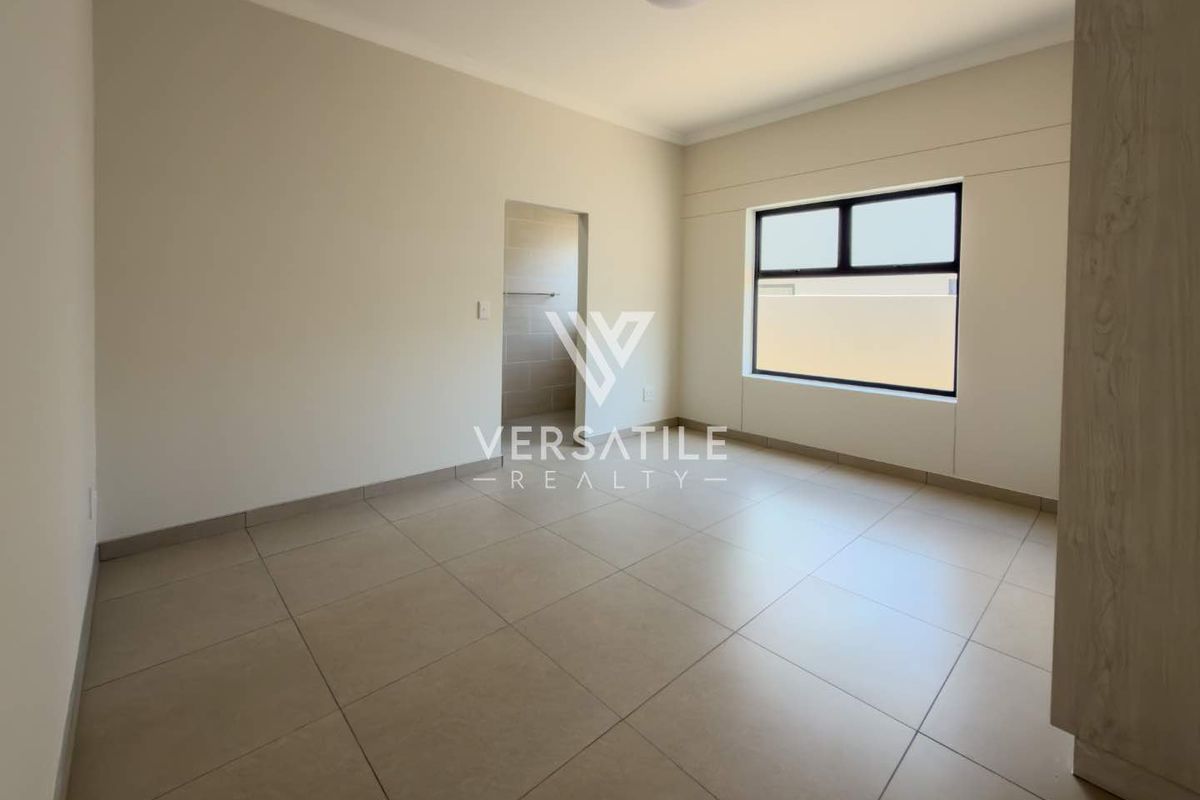 A bright, empty bedroom featuring neutral tiled flooring, clean walls, and an en-suite bathroom entrance.