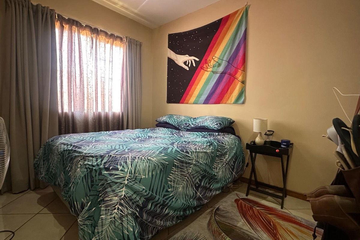 A cozy bedroom featuring tiled flooring, neutral wall tones, and a window with installed curtain tracks.
